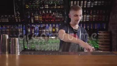 年轻的调酒师调酒师把许多冰块放进玻璃里，然后在漂亮的现代酒吧里做鸡尾酒